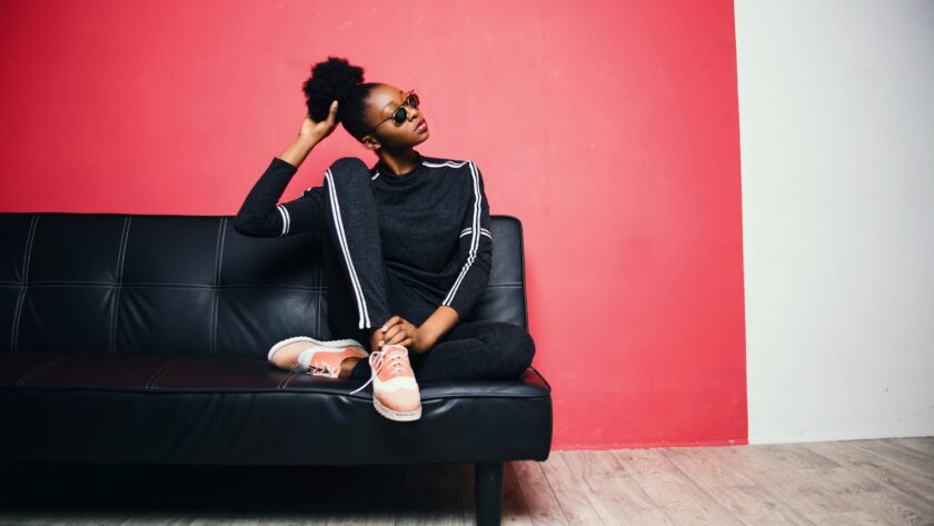 streetstyle loungewear, woman with black and white sweater with pants sitting on black leather sofa beside red painted wall, Spring 2023, Spring 2023 ootd